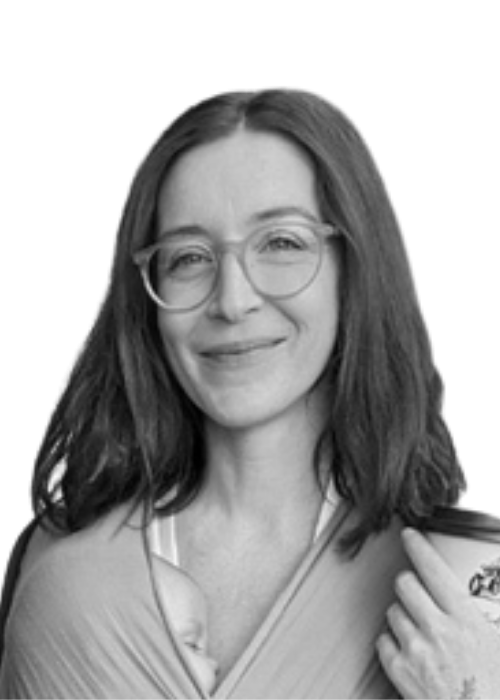 Smiling woman with round glasses holding a baby wrapped in cloth (grayscale photo).