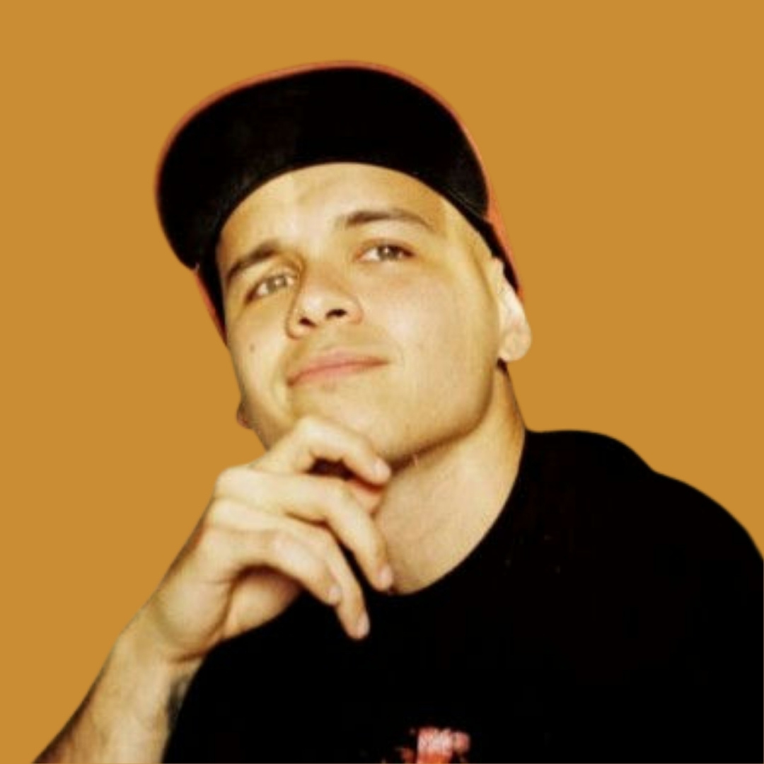 Portrait of a young man wearing a black cap and black shirt, resting his chin on his hand against an orange background.