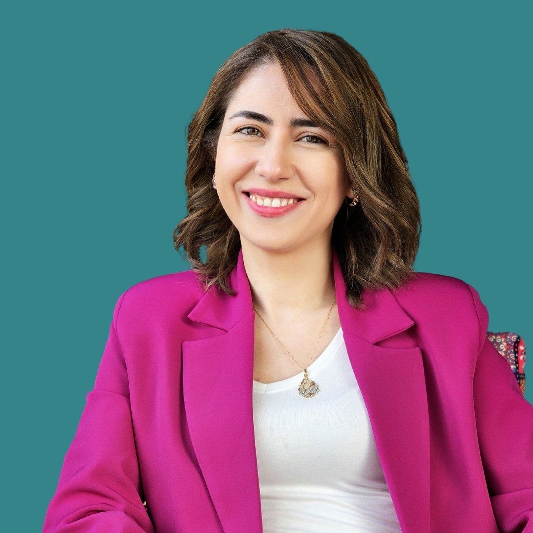 Woman smiling in a magenta blazer over a white top, teal background.